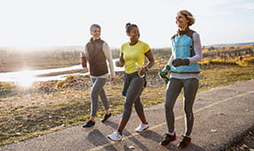 Three women power walking on a sunny path in a park
