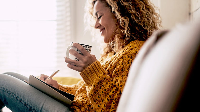 Woman writing in a journal and drinking a cup of tea