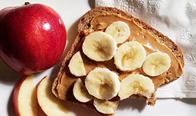 Peanut butter and banana on whole wheat bread alongside apple slices