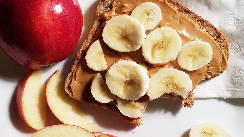 Peanut butter and banana on whole wheat bread alongside apple slices