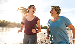 Mother and daughter having fun, jogging together along a river