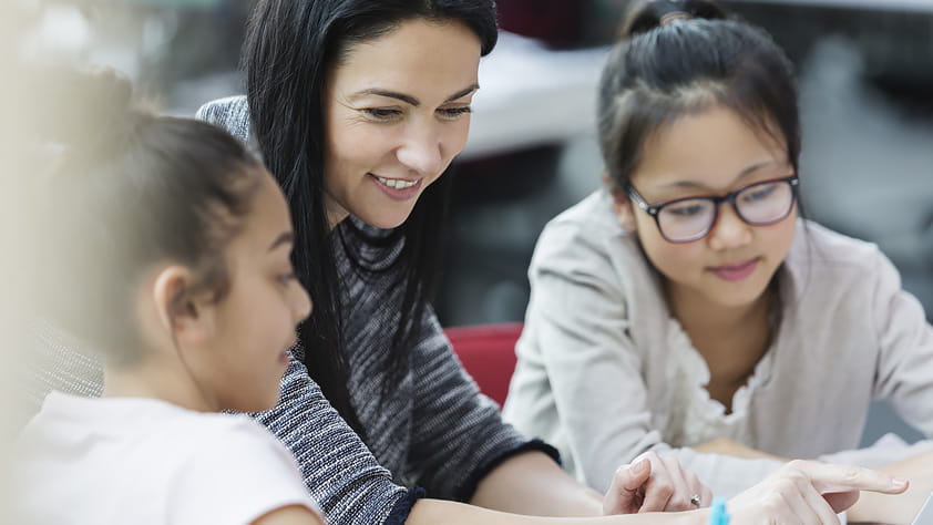 Female teacher and students using a laptop in their classroom