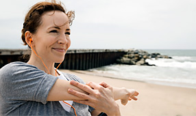 Smiling woman listening to music and stretching her arm while on the beach