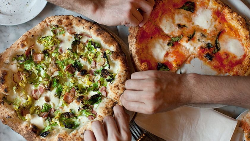 Close-up of hands reaching for two kinds of healthy pizza