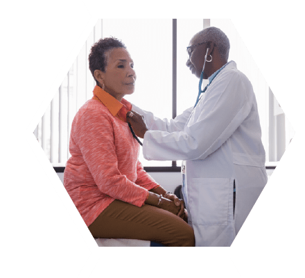 Middle aged woman in a doctors visit while a doctor checks breathing with a stethoscope