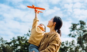 Young female NEA member and little daughter spending time together outdoors, playing with airplane toy