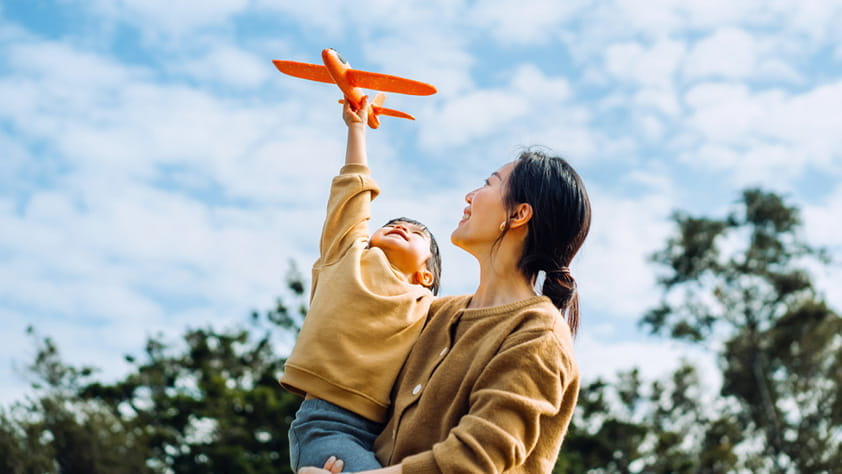 Young female NEA member and little daughter spending time together outdoors, playing with airplane toy