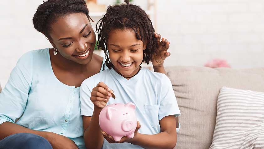 Mother and Young Daughter Putting Coins Into Piggy Bank