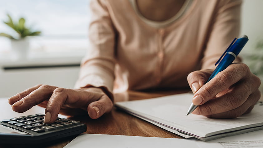 Woman sitting at a table using a calculator and writing on a notepad