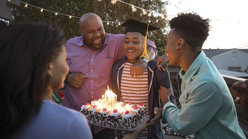 Family celebrating their son's graduation with cake on their backyard deck