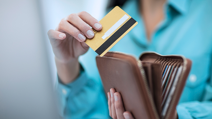 Close-up of a woman in a turquoise shirt taking a credit card out of her wallet