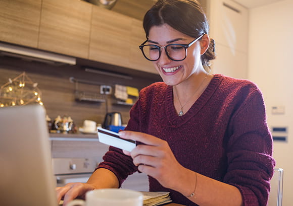 Young woman holding a credit card and shopping from home on her laptop