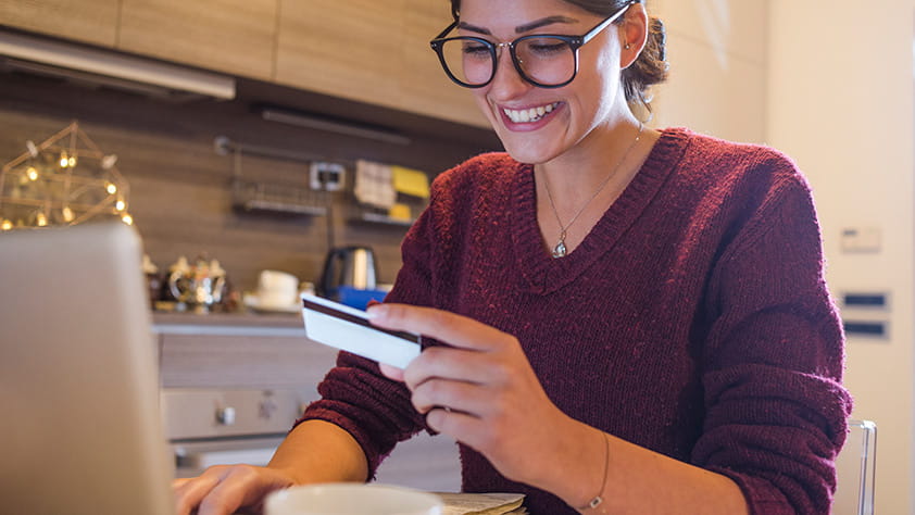 Young woman holding a credit card and shopping from home on her laptop