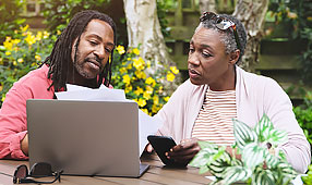 Senior Couple Using a Laptop and Going Over Paperwork Outside in the Garden at Home