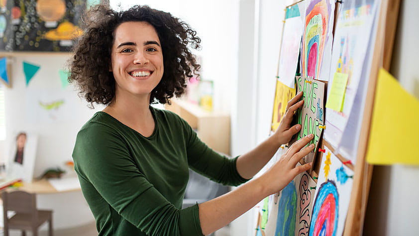 Teacher Making Bulletin Board at School, Smiling and Looking at Camera