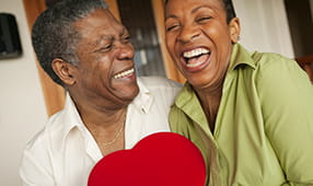 Happy African-American older couple holding a bright red heart-shaped box of chocolates