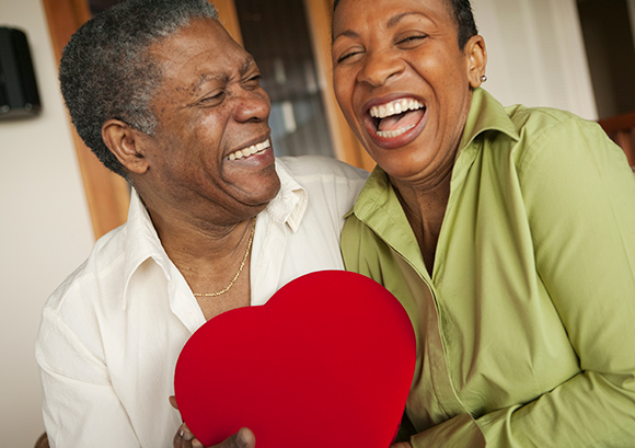 Happy African-American older couple holding a bright red heart-shaped box of chocolates