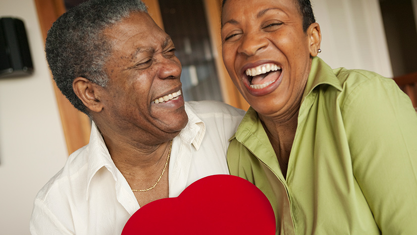 Happy African-American older couple holding a bright red heart-shaped box of chocolates
