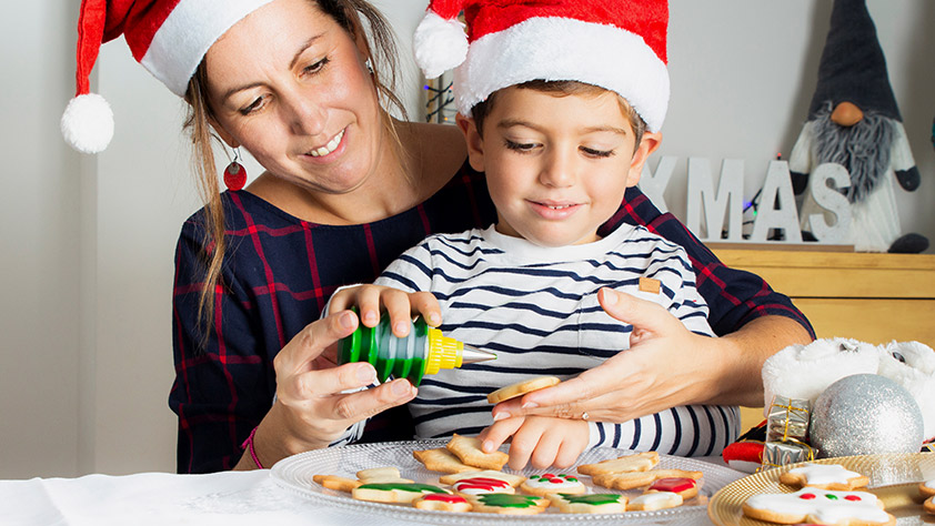 Mother and young son wearing Santa hats and decorating cookies
