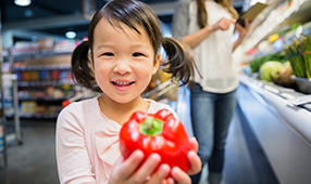 Close Up of Asian Girl Holding Red Pepper in Grocery Store