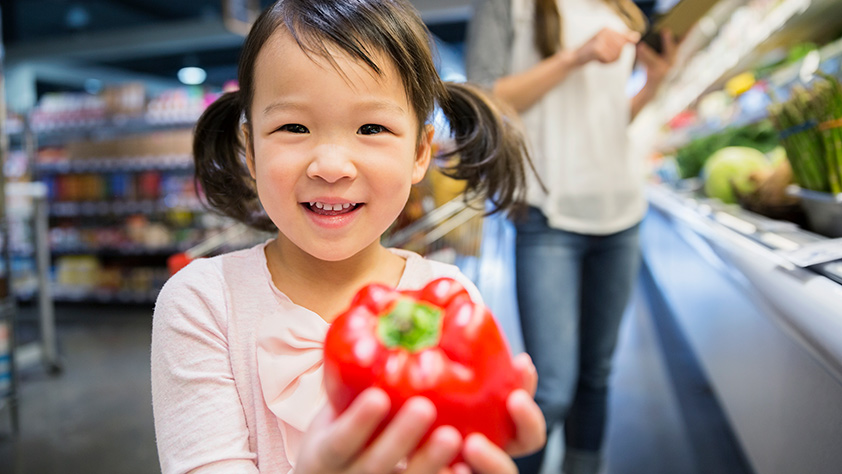 Close Up of Asian Girl Holding Red Pepper in Grocery Store