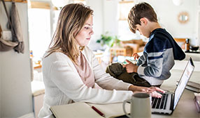 Woman working from home on laptop while son uses smartphone