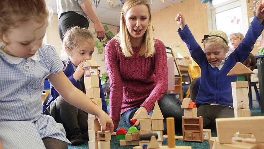Teacher and young students stacking wooden blocks in a school classroom