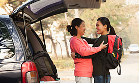Mother and daughter embracing behind a car full of her things on a college campus