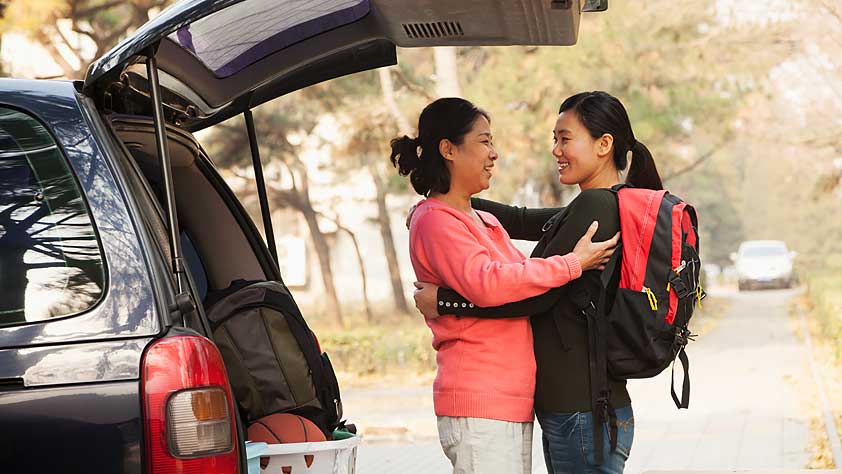 Mother and daughter embracing behind a car full of her things on a college campus