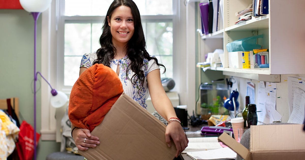 Young woman holding a box and moving into her college dorm room