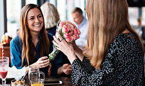 Woman Receiving Bouquet of Flowers from Female Friend