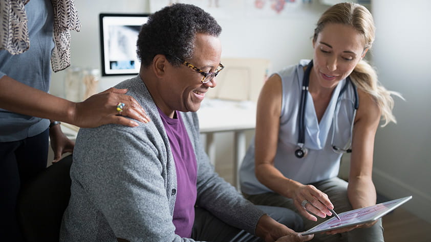Female doctor showing a digital tablet to a senior male patient in an examination room