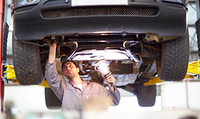 Auto Technician Inspecting Undercarriage of Car