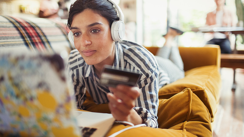 Woman with Headphones on Laying on Couch Making an Online Purchase