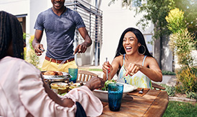 Happy family eating a meal seated around their backyard picnic table