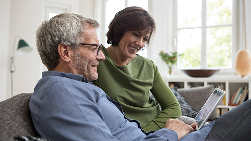 Middle Aged Couple on Couch Looking at Tablet