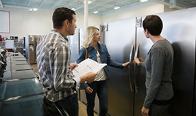 Saleswoman helping a couple shopping for a refrigerator in an appliance store