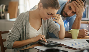 Concerned Couple Looking Through Paperwork and Using a Calculator