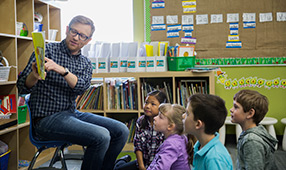 Male Elementary Teacher Reading Story to Children