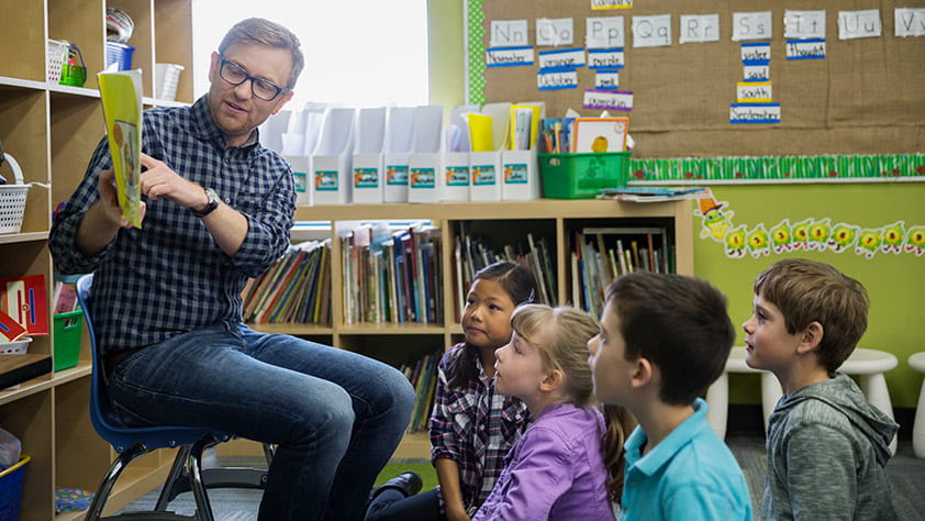 Male Elementary Teacher Reading Story to Children