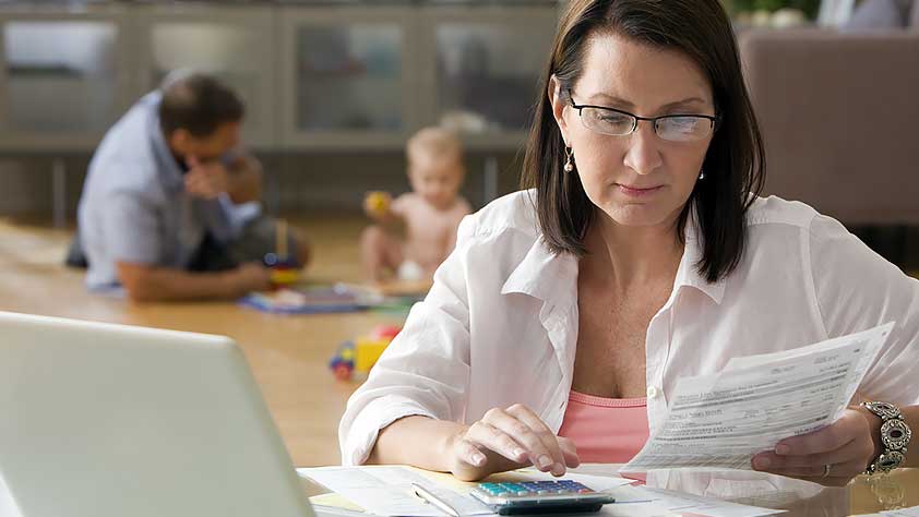 Tips to Help Teachers Manage a Financial Emergency - Woman Calculating Bills with Her Family Playing in the Background