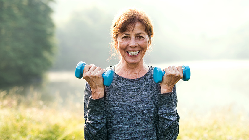 Senior woman lifting small blue hand weights outdoors