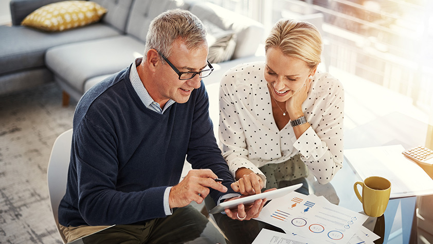 Mature couple using a digital tablet while going through financial paperwork at home