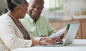 Senior African-American husband and wife using their laptop and reading a paper document