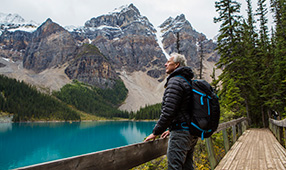 Senior Man Wearing a Hiking Backpack Standing on Boardwalk Admiring Mountain