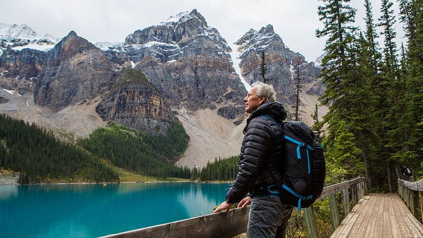 Senior Man Wearing a Hiking Backpack Standing on Boardwalk Admiring Mountain - Freebies and Discounts Especially for Seniors