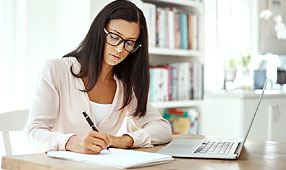 Young Woman Using a Laptop and Writing Notes