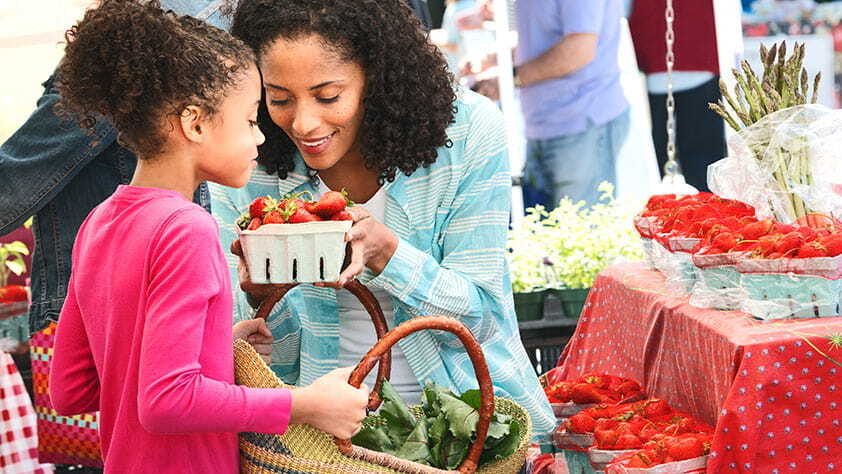 Mother and daughter smelling strawberries at farmers market