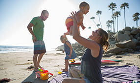 Young family of four playing on a sunny beach with palm trees in the background