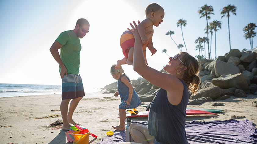 Young family of four playing on a sunny beach with palm trees in the background